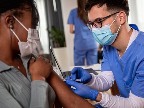 Male nurse with mask giving vaccine to patient in clinic. Male nurse with mask giving vaccine to patient in clinic.